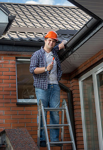 微笑的木匠在屋顶下用锤子梯上装模作样图片