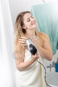 美丽的女人躺在浴巾里室用吹毛机洗发图片