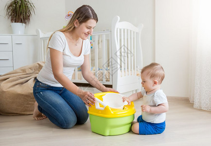 年轻微笑的母亲坐在起居室的地板上教女婴如何使用室内锅图片