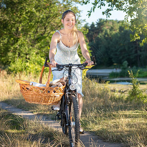 美丽女子骑着自行车带着野餐篮子去公园图片