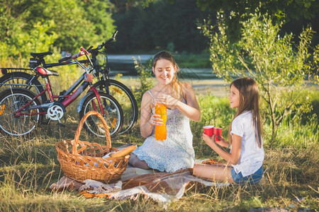 母亲在河边和女儿一起野餐母亲在女儿和杯中倒橙汁图片
