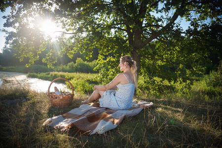 美丽的女人躺在树下的毛毯上放松看着日落图片