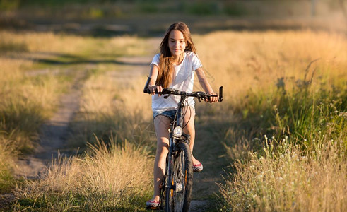 日落时在草地骑自行车的微笑女孩图片