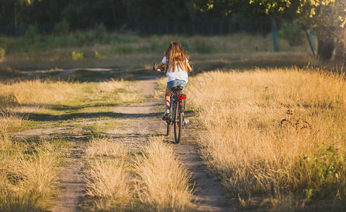 妇女骑自行车在草地上的泥土路图片