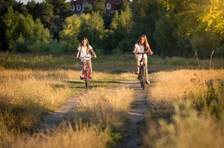 日落时两名少女在草地上骑自行车图片