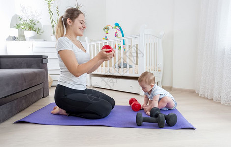 母亲和她的婴儿子坐在家里健身垫子上与哑巴一起运动图片
