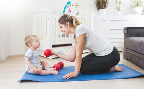 微笑的母亲在客厅地板上与婴儿一起做体操图片