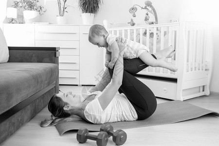 美丽的年轻母亲和她男婴在客厅地板上做瑜伽的黑白画面图片