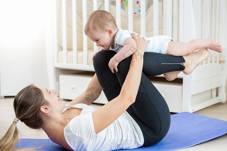 微笑的女人在客厅与婴儿一起做瑜伽锻炼图片