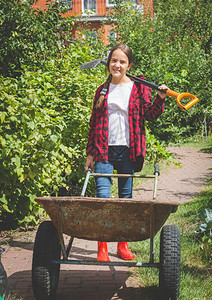 快乐的年轻女孩在花园里摆着手推车和铲子图片