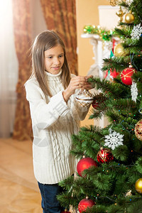 穿着羊毛衣的快乐少女在家里装饰圣诞树图片