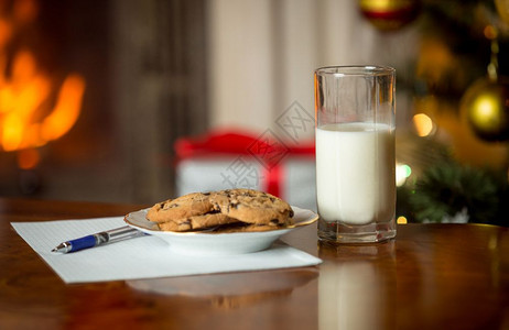 在烧火壁炉和圣诞树旁边的桌子上为圣诞老人提供的饼干牛奶和信件图片