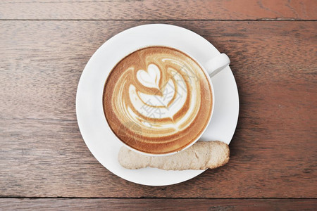 咖啡拿铁心型在一个白色杯子和饼干木制背景图片