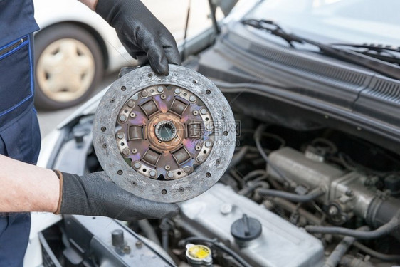 戴手套的汽车机械师将旧离合盘套在汽车发动机上图片