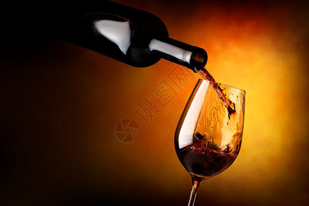 红酒倒在橙色背景的葡萄酒杯中图片