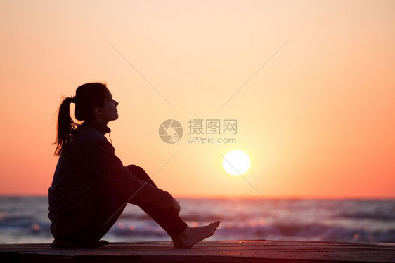 寂寞女孩坐在日出沙滩上女人在日出天空上摇欲坠图片