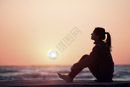 寂寞女孩坐在日出沙滩上女人在日出天空上摇欲坠图片
