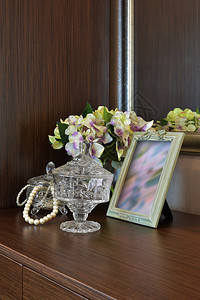 木制桌上有图画框和鲜花的珠宝水晶罐图片