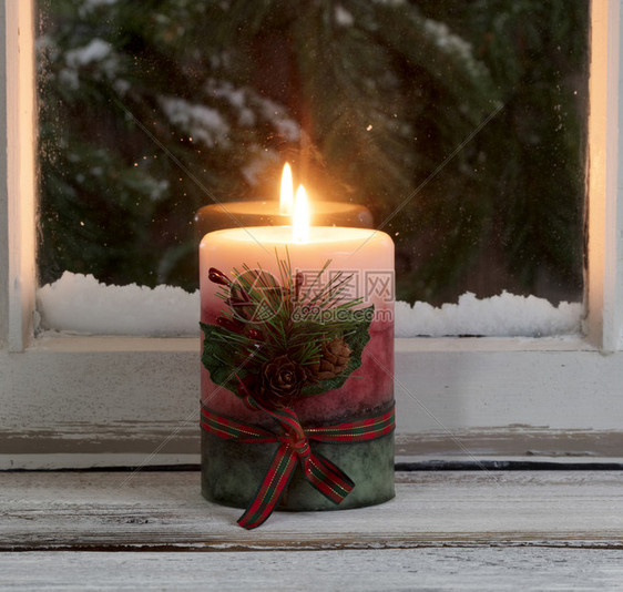 圣诞蜡烛在窗边照亮背景是雪的长青树枝图片