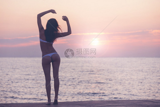 美丽的女孩站在日出海滩上女人在日出的天空上摇欲坠图片