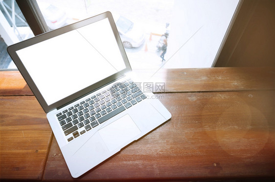 办公室窗口前的木制桌子上有空白屏幕的笔记本电脑图片