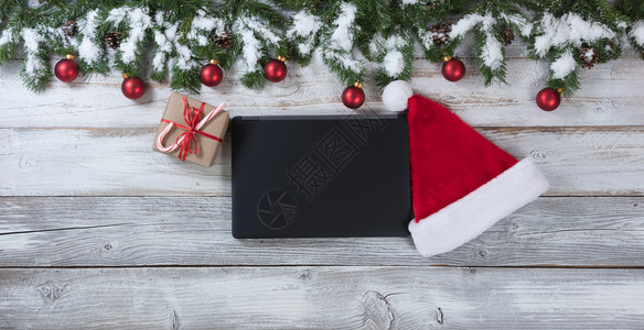 圣诞背景有老人帽电子笔记本和礼物有传统装饰品印在生锈的白木上图片