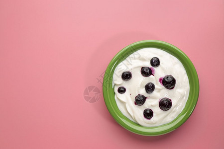 活有机希腊酸奶香草和蓝莓在粉红背景的绿色陶瓷碗里图片