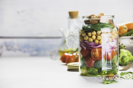健康素食能提振沙拉配有鸡豆西红柿洋葱菠菜和坚果玻璃罐混凝土背景选择焦点图片