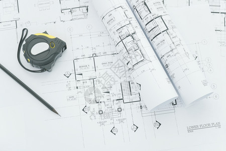 建筑师工作场所建筑蓝图上面有测量胶带安全头盔和桌面上的工具图片