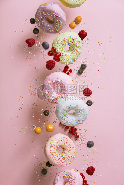甜圈喷洒和浆果在粉色糊面背景下落或飞起来图片