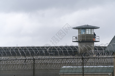 一名武装警卫从个监狱守望塔的栏杆上对地面进行勘察背景图片
