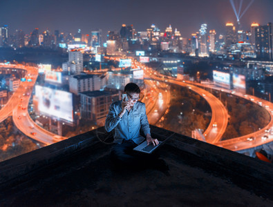 亚洲男子使用具有城市背景技术通讯概念的电话和笔记本脑亚洲男子使用具有城市背景的电话和笔记本脑技术图片