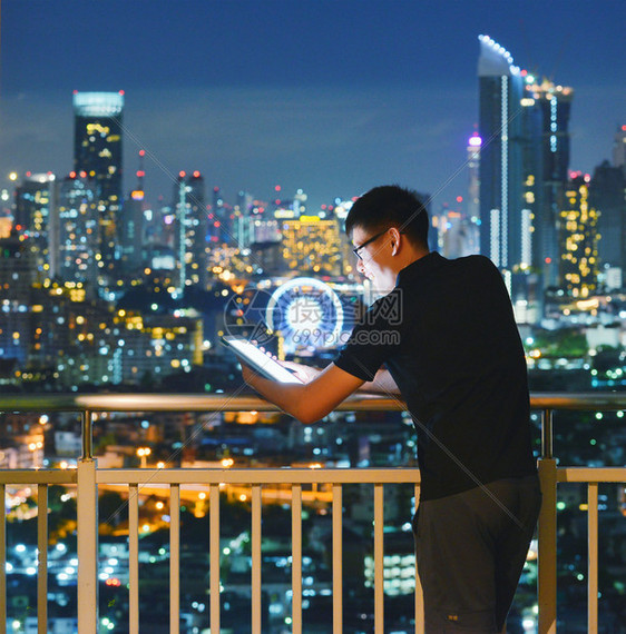 亚洲男子在带有曼谷城市背景的阳台使用平板图片