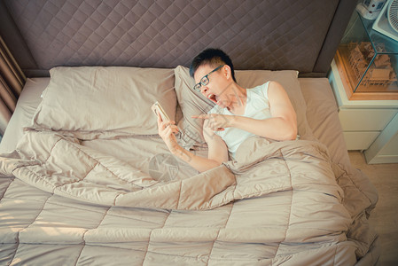 愤怒的亚洲男人责怪床上的电话图片