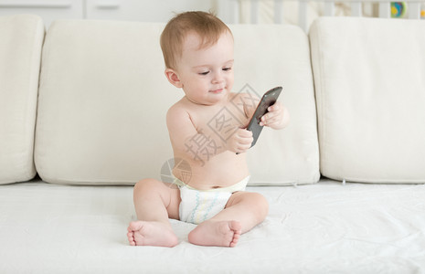 坐在沙发上并使用智能手机的尿布中可爱婴儿男孩坐在沙发上并使用智能手机的婴儿男孩坐在沙发上并使用智能手机的尿布中婴儿男孩图片