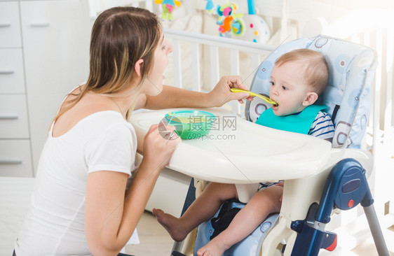 10个月大的婴儿男孩坐在高椅子上吃勺里的粥图片