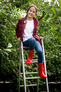 穿着红色橡皮靴的美丽女孩坐在花园的梯上图片