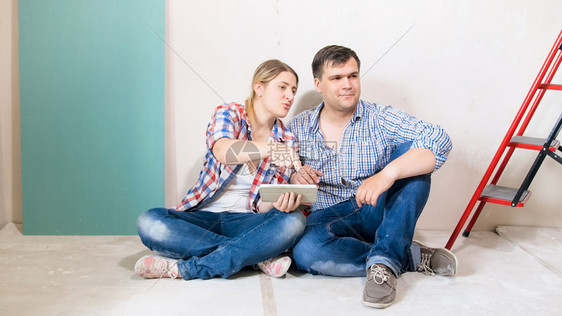 幸福的情侣坐在他们新房子的地板上从网商店中选择家具图片