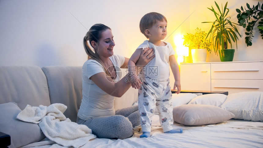 穿着睡衣的可爱小男孩和年轻微笑的母亲在睡觉前床上图片