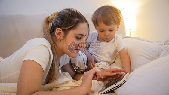 微笑的年轻母亲在数字平板电脑上浏览互联网图片