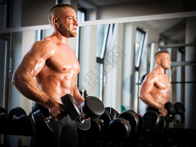 肌肉强壮的男人和镜子旁边的哑铃一起工作手臂训练在健身房里举重运动和健美的概念肌肉男人在健身房里工作图片