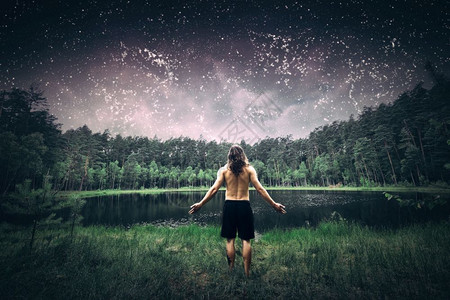 年轻人站在森林里手臂张开梦见了充满星湖和树林的夏夜天空自然和由的概念夜晚站在森林里图片