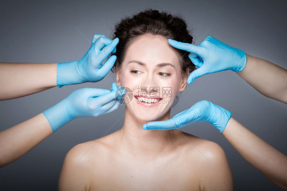 在整容手术前进行皮肤检查的微笑妇女用手套测量和触摸妇女脸部的手用皮肤检查的微笑妇女用手套测量和触摸妇女的脸部图片