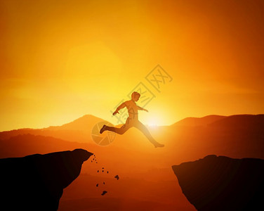 人从一块岩石跳到另日落山脉景色危险沙兰格胜利勇敢的决定概念图片