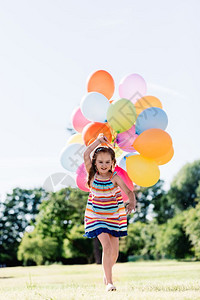 快乐的小女孩带着一堆多彩的气球跑来去图片
