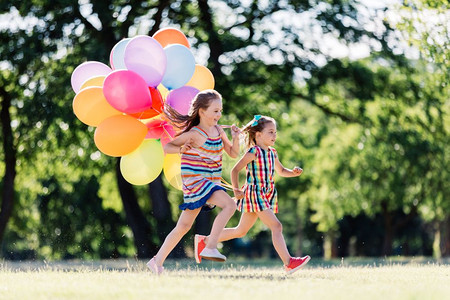 两个快乐的女孩在公园里跑来去带着一群多彩的气球友谊概念两个快乐的女孩带着一堆多彩的气球跑来去图片