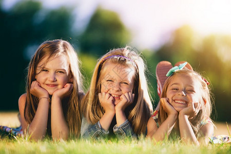 三个微笑的小女孩躺在公园的草地上图片