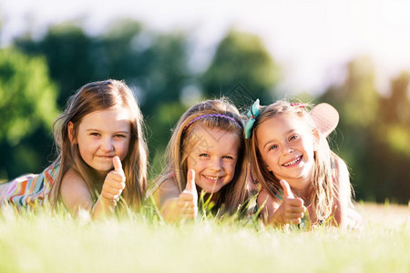 三个微笑的小女孩躺在公园的草地上图片