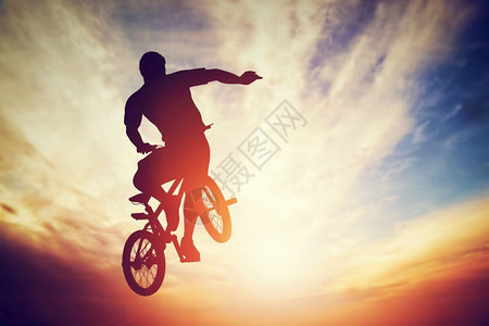 男人骑着Bmx自行车跳跃玩着对抗日落天空的把戏图片