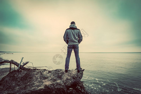 中年男子站在荒野海滩上的破树望远海平线传统概念图片